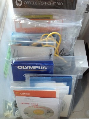 box full of zipper bags containing computer cords, disks, and booklets