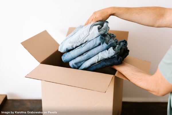 A person's hands placing a stack of clothing into a cardboard moving box showing how to successfully pack moving boxes.