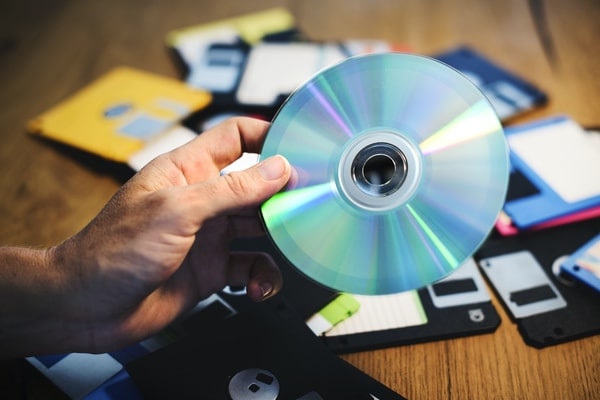 digital assets - hand holding CD with floppy disks in background on table