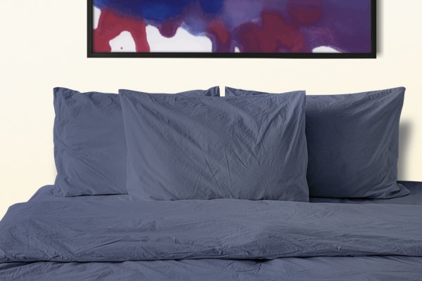 bed with blue sheets and blankets with picture above bed on off-white wall