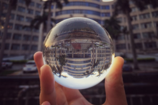 hand in front of office building holding crystal ball with upside down view of building indicating paradigm shiftde down image of