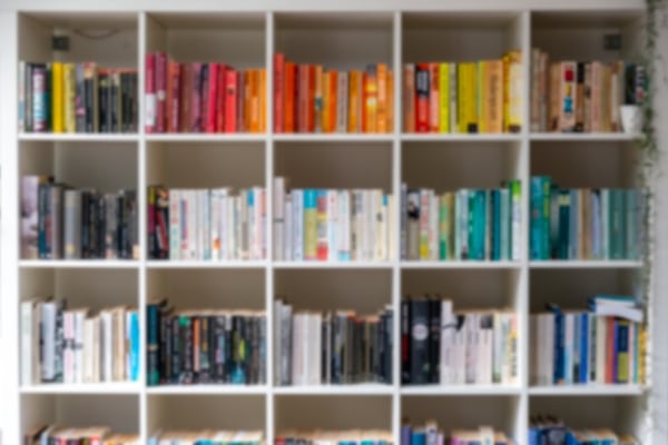 Blurred image of white wooden bookcase filled with books organized by colour to create home envy