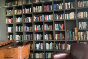 book collection displayed on shelves behind leather chair and grand piano