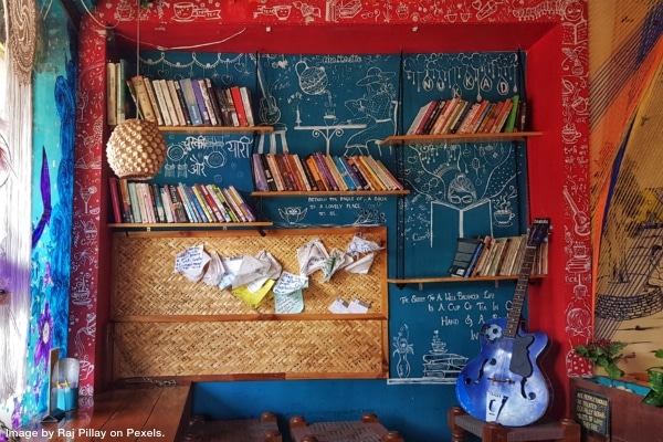 Room with blue and red wall with full bookshelves and papers stuck to the bulletin board and a guitar in the corner representing minimalism vs maximalism