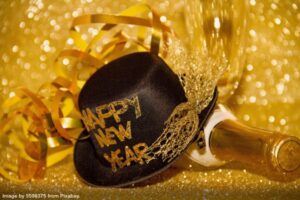 black bowler hat with happy new year written on it lying on a champagne bottle with gold streamers in the background representing an alternative to new year's resolutions