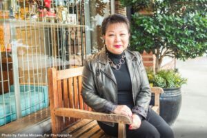 Linda Chu, professional home organize and move manager in Vancouver BC sitting on a bench smiling at the camera for Neighbours of Edgemont Magazine